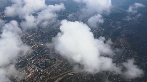 Aerial View From Airplane Window at High Altitude of Distant City Covered with Puffy Cumulus Clouds