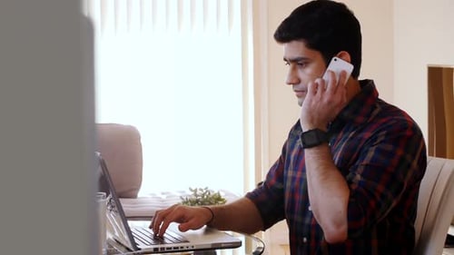 Young Adult Works on Laptop While Talking on Phone