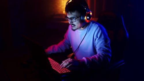 Male gamer plays videogames on laptop and loses, squeezes head with hands in frustration, side view.