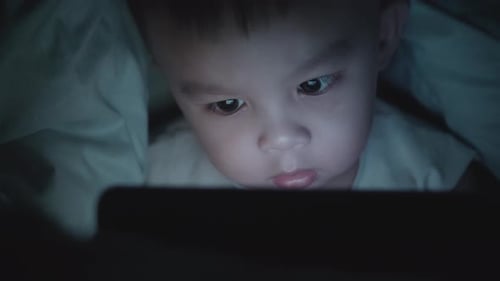 Petit garçon asiatique regardant une tablette sur le lit