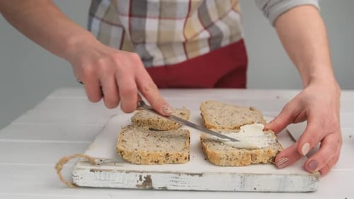 Woman Spreads Cream Cheese onto Sliced Grain Bread