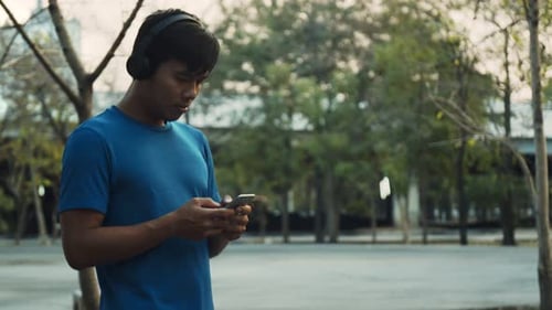 Asian men resting after training outdoors using smartphone while walking in the park environment.
