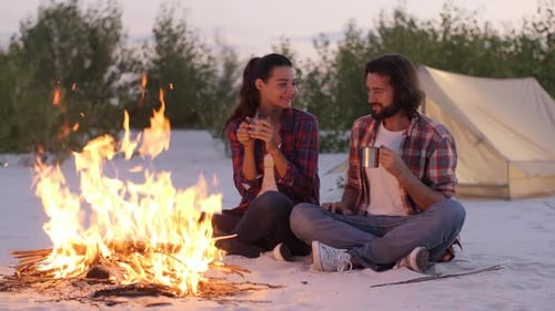 Young Couple Camping on Sandy Beach with Campfire
