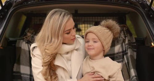 Mother and Child Embrace in Car Trunk During Autumn