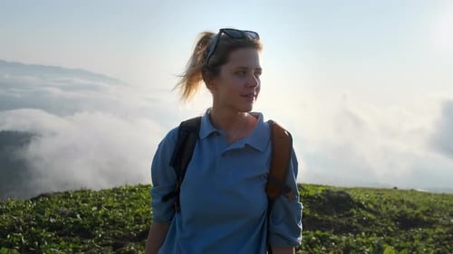 Teen Girl Hiker at Top of Mount Standing Above Clouds and Looking at Camera