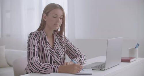Woman Writing at Desk With Laptop Computer