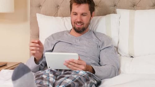 Man Relaxes in Bed Using Tablet