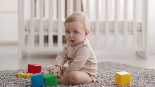 Cute Infant Baby Boy Sitting On Floor And Playing With Building Blocks