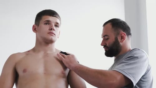 Osteopath Doing Kinesiology Taping on Patient's Shoulder in Clinic