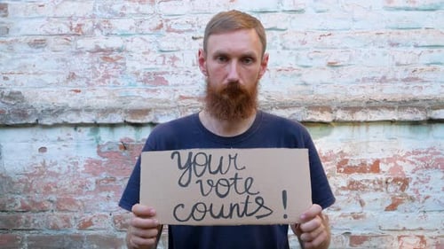 Bearded Man Holds Vote Sign in Front of Brick Wall