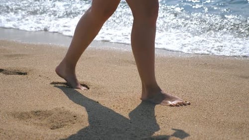 Close Up of Female Feet Walking on Golden Sand at the Beach with Ocean Waves at Background