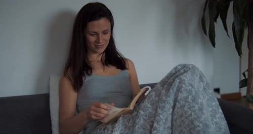 Woman Reading Book on Sofa Covered in Blanket