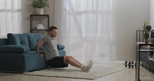 Adult Sporty Man Is Training at Home Using Furniture As Gym Equipment Workout in Living Room Leaning