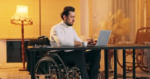 Man in Wheelchair Works on Laptop at Desk