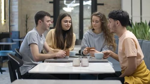 Young Adults Toasting Mugs at Cafe Table