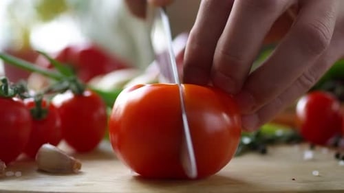 Cerca de las manos del cocinero masculino cortando el tomate en dos mitades