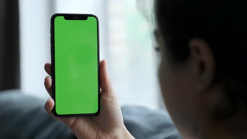 Close-up shot of green screen template smartphone in female hands at home, girl is watcing