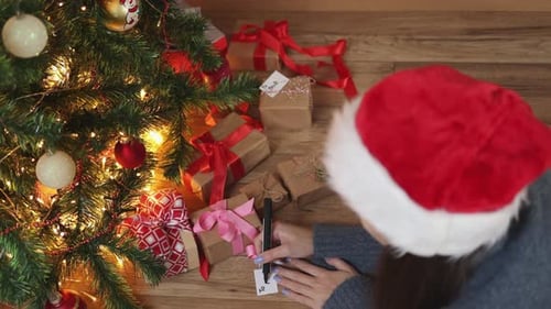 Woman Writes Gift Tags Under Christmas Tree