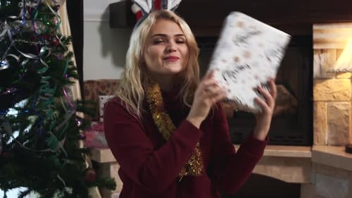 Young Woman Holds Christmas Gift Near Fireplace