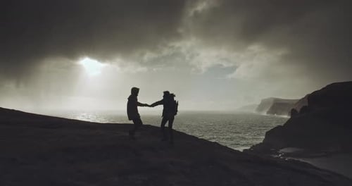 Silhouetted Figures Holding Hands Near Dramatic Ocean