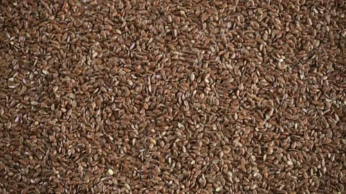 Flax Seeds Being Poured from Wooden Bowl