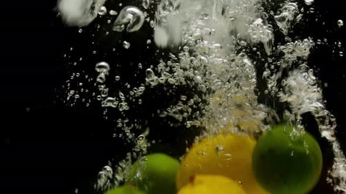 Closeup of Falling Ripe Lemons Oranges and Limes Into Sparkling Water on Black Background Making