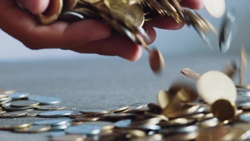 Hand Drops Pile of Gold and Silver Coins