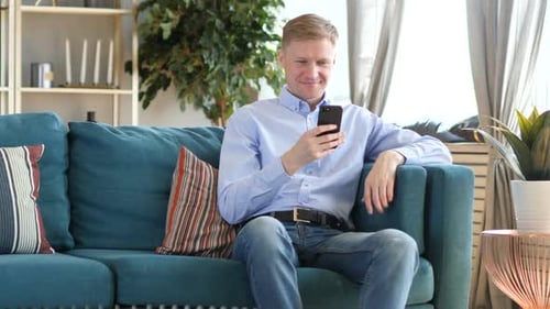 Young Man Relaxing on Sofa Using Mobile Phone