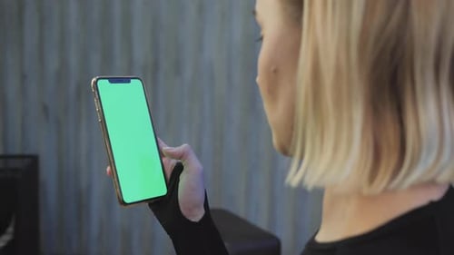 A Young Athletic Woman Holds A Smartphone in Her Hand, Shows A Green Chromakey Screen, Is in The Gym