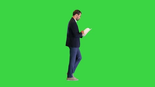 Serious Young Businessman Reading Documents While Walking on a Green Screen Chroma Key