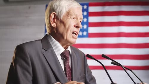 Mature Man Giving Speech with American Flag Backdrop