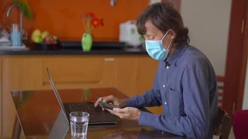 A Young Man Wearing a Face Mask Works From Home During Coronavirus Self-isolation. He Talks on a