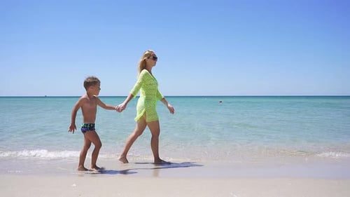 Little Boy Walks Along the Sandy Shore of the Azure Sea Holding His Mother's Hand.