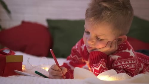 Young Boy Writes Christmas Letter on Bed