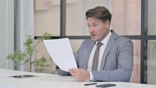 Middle Aged Man Upset while Reading Documents in Office
