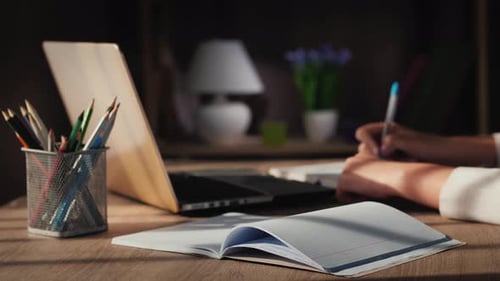 Student Writes in Notebook at Desk with Computer