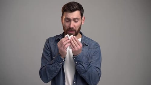 Man Sneezing and Holding a Tissue Looking Sad