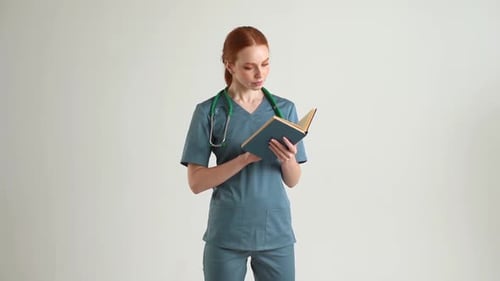 Portrait of Focused Young Woman Intern in Green Uniform with Stethoscope Reading Medical Academic