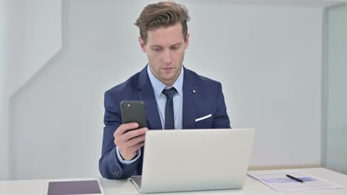 Man Uses Phone While at Computer