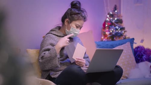 Woman With Mask Uses Laptop By Christmas Tree