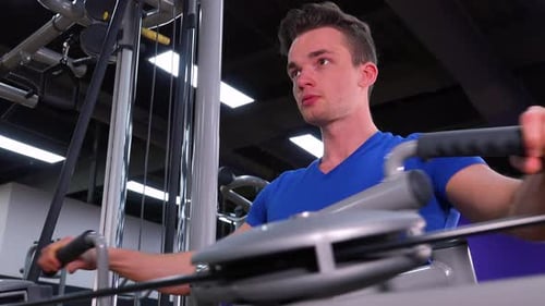 A Young Fit Man Trains on a Machine in a Gym - Closeup From Below