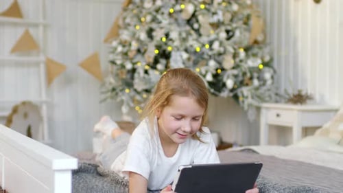 Girl Using Tablet on Bed Near Christmas Tree
