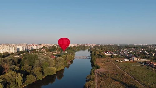 A beautiful red balloon flies in the evening over the river and the city.