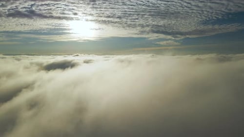 Aerial view of bright yellow sunset over white dense clouds with blue sky overhead.