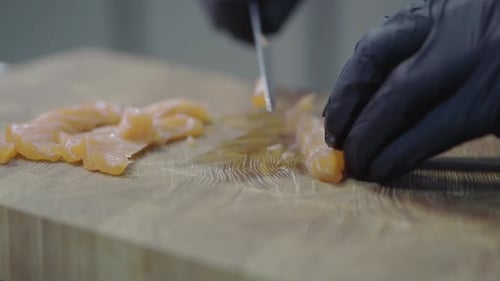 Chef in Black Rubber Gloves Cutting Salmon on the Wooden Board in Modern Restaurant
