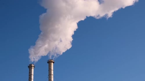 Industrial Chimneys Spewing Smoke Against Blue Sky