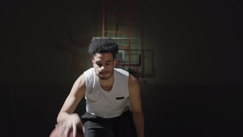 Male Basketball Player Dribbling Ball on Dark Court