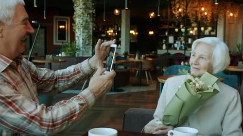 Senior Man Taking Pictures of Elderly Woman Using Smartphone Camera in Cafe