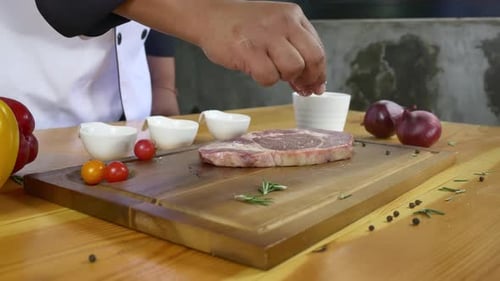 Chef cook season fresh chunk of deli piece of beef with sea salt and grounded spicy peppers.