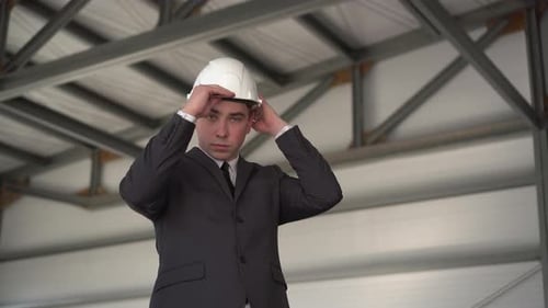 Un jeune homme met un casque de protection et montre son pouce sur un chantier de construction. Le patron en costume
